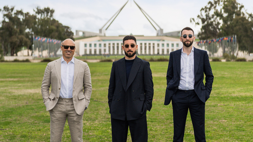 three men standing outside Parliament House in suits