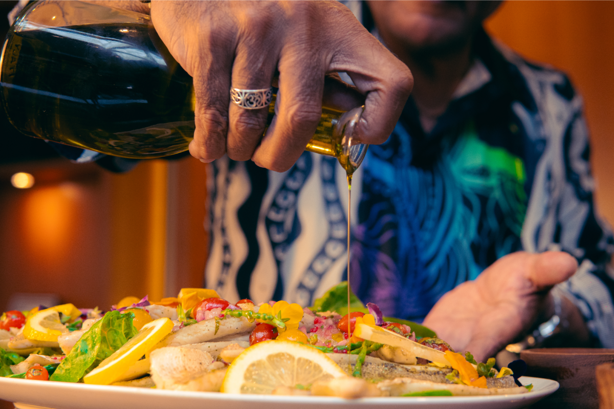 a hand pouring olive oil over a plate of fish and vegetables