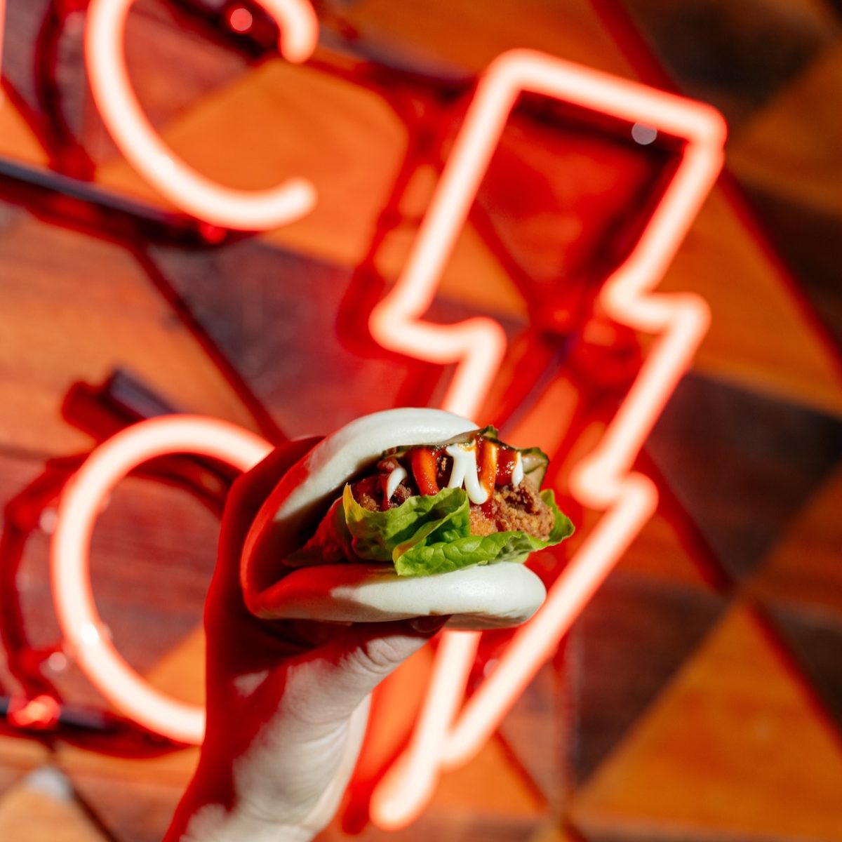 A white hand holding a bao bun against a light fitting in the shape of a lightening bolt.