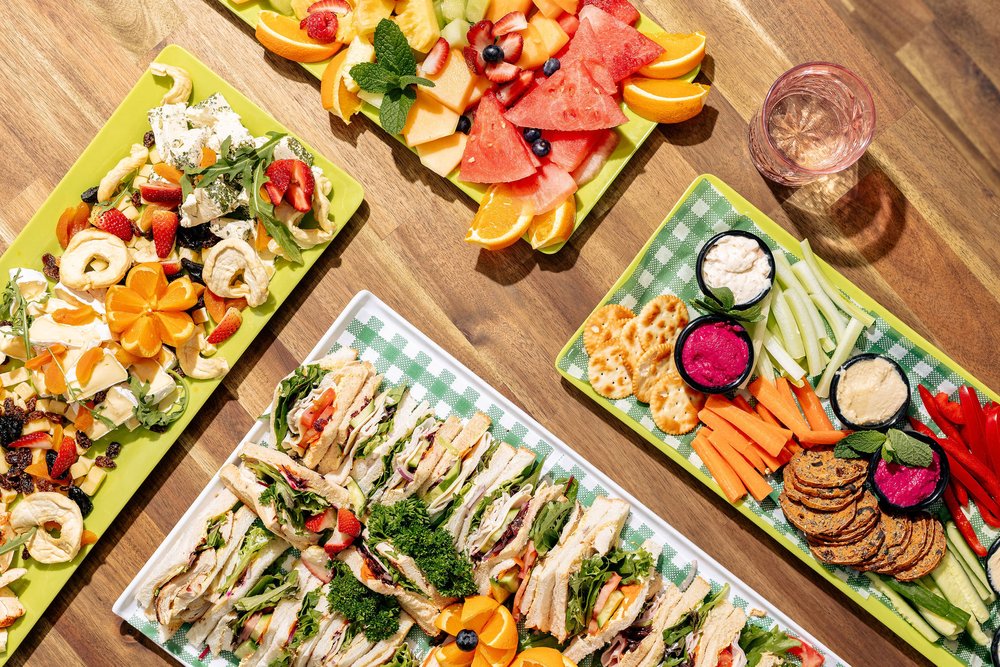 four platters of food including sandwiches, fruit and crackers