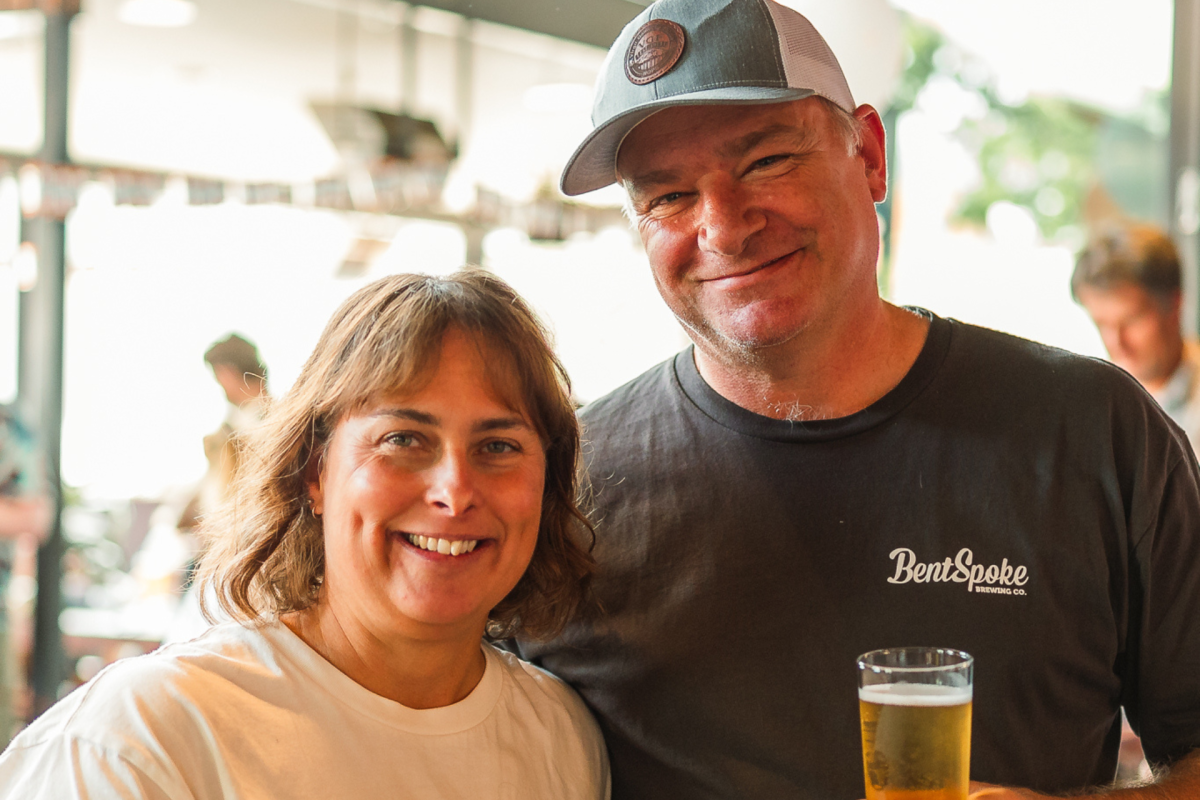 A man and a woman standing side by side, man with beer.