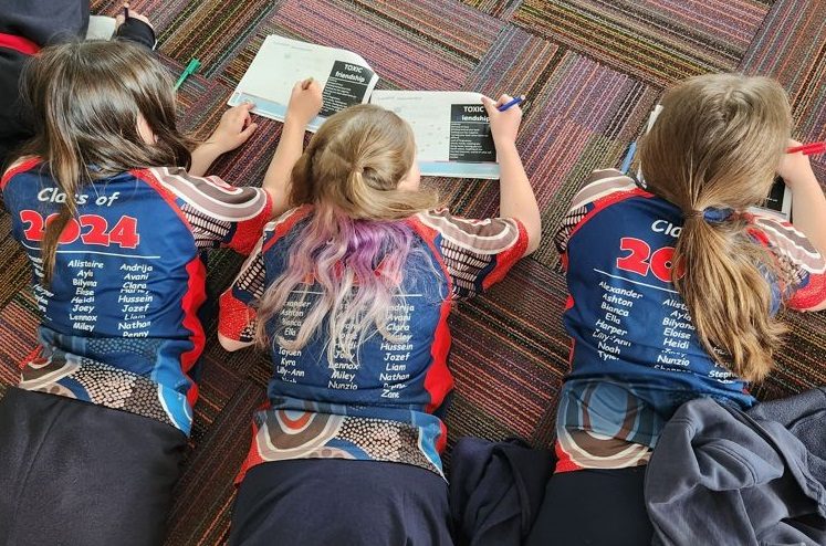 three children lying on a floor writing in a book