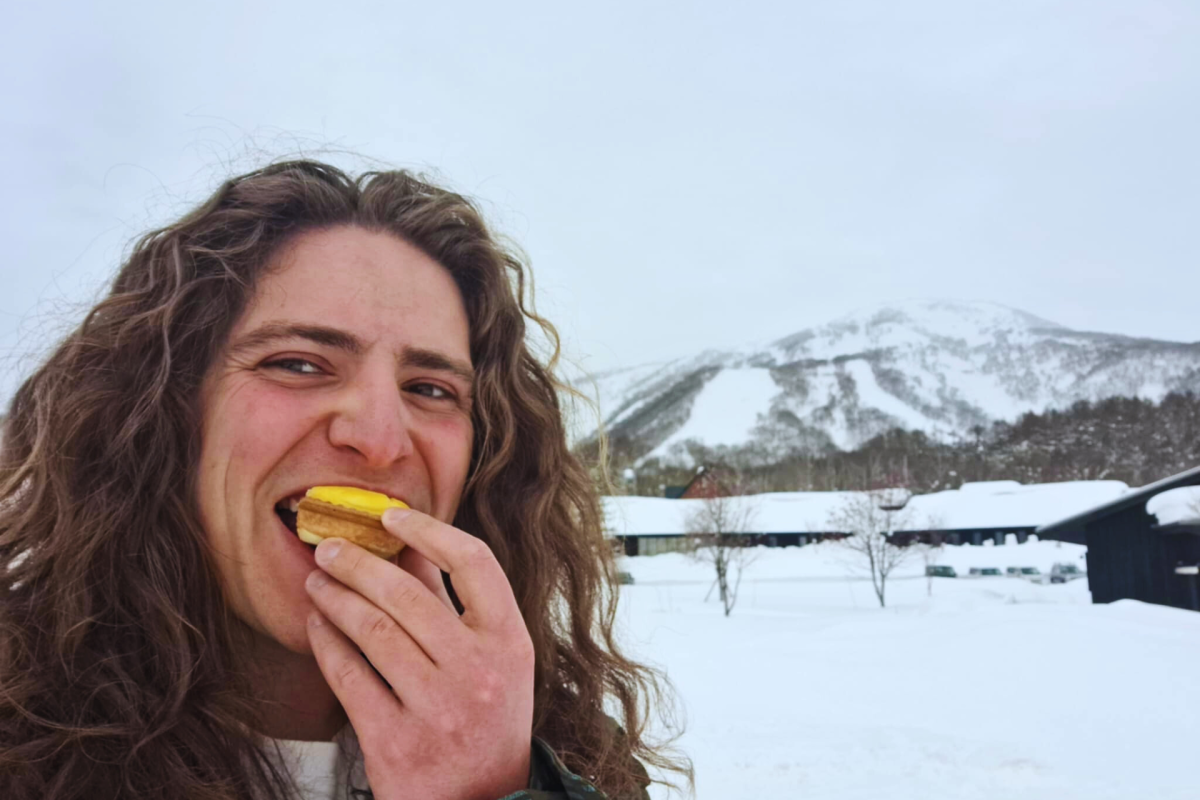 Man eating a cheese tart in front of a snowy mountain