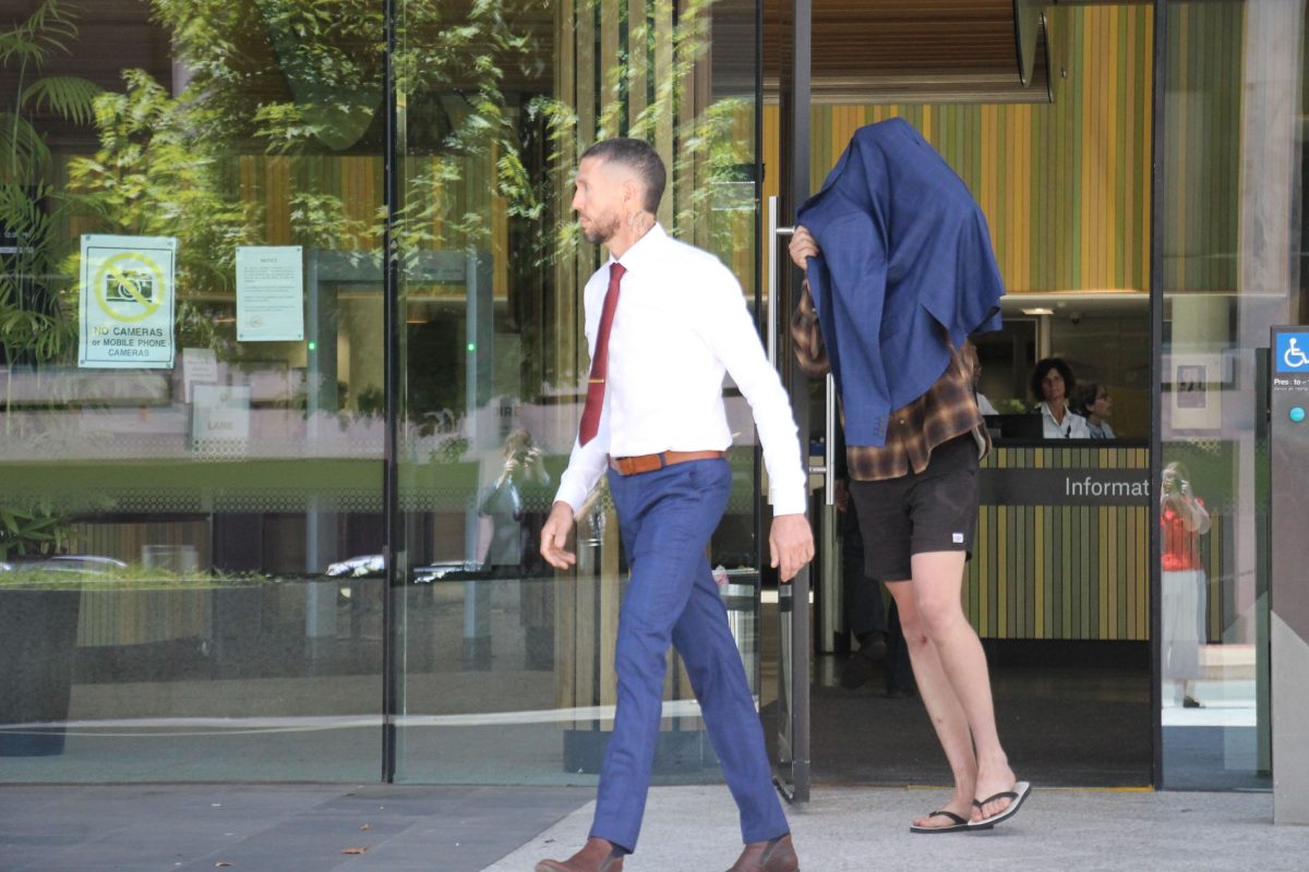 A man in a suit and a man in shorts covering his face