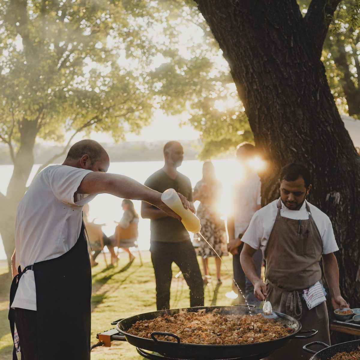 Two chefs cooking paella outdoors in the sunshine.