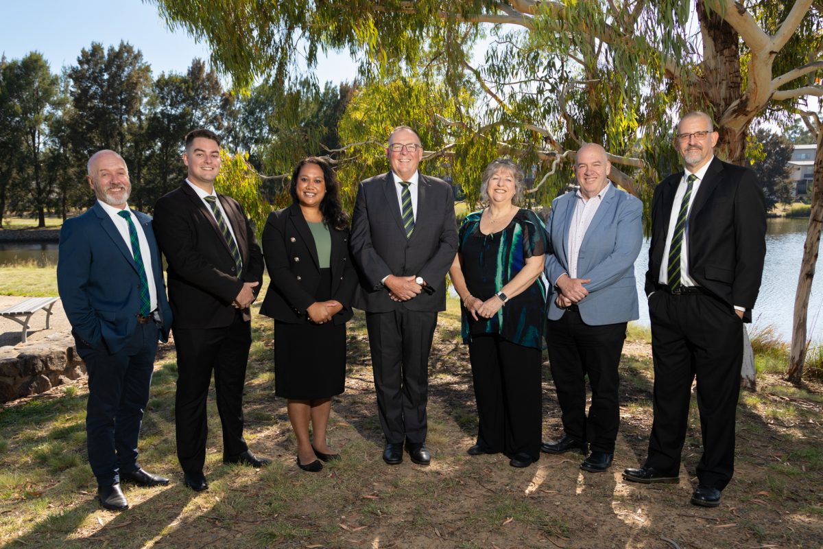 McIntyre Property sales team standing outside in front of a large gum tree and Lake Tuggeranong