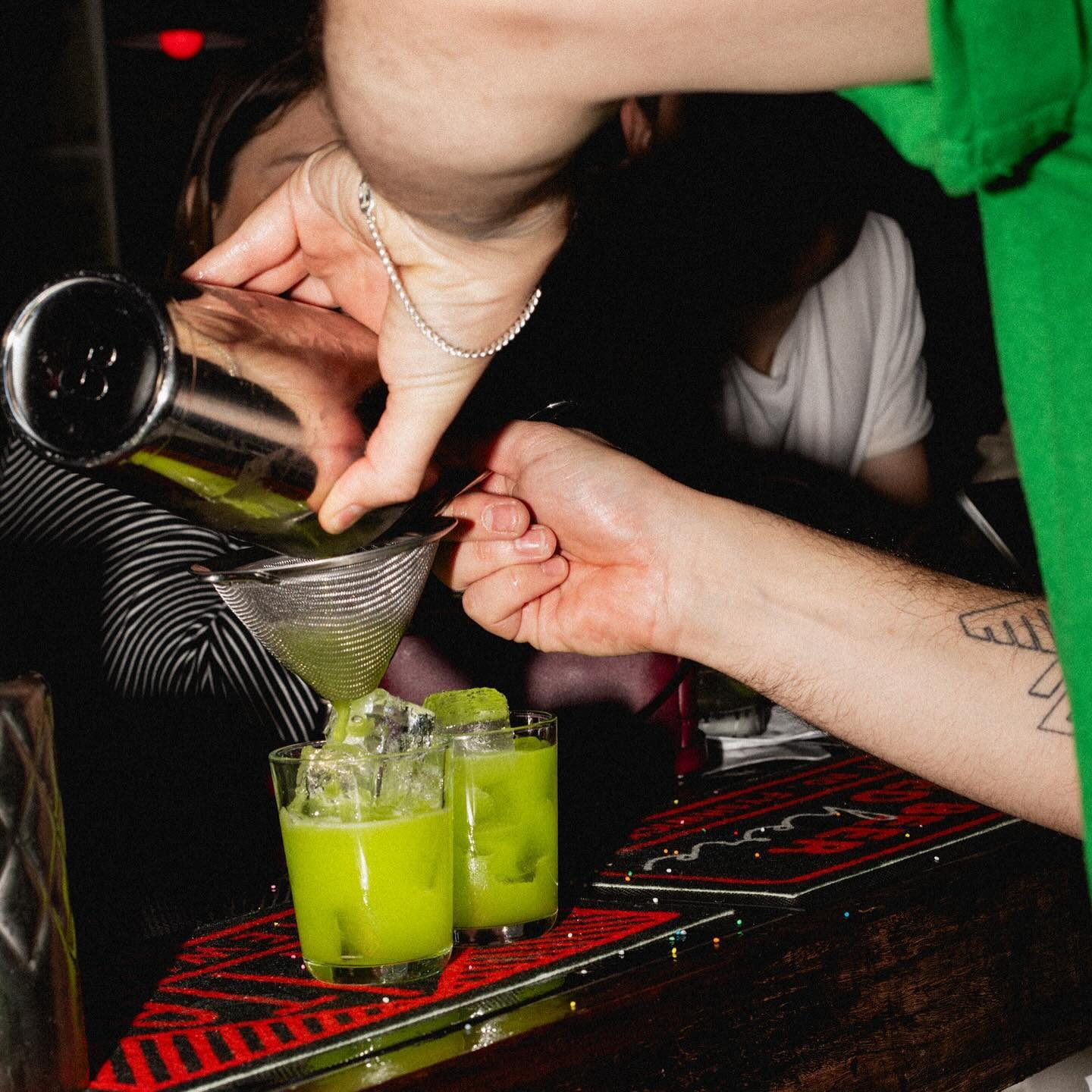 A bartender pours green drinks into small tumblers.