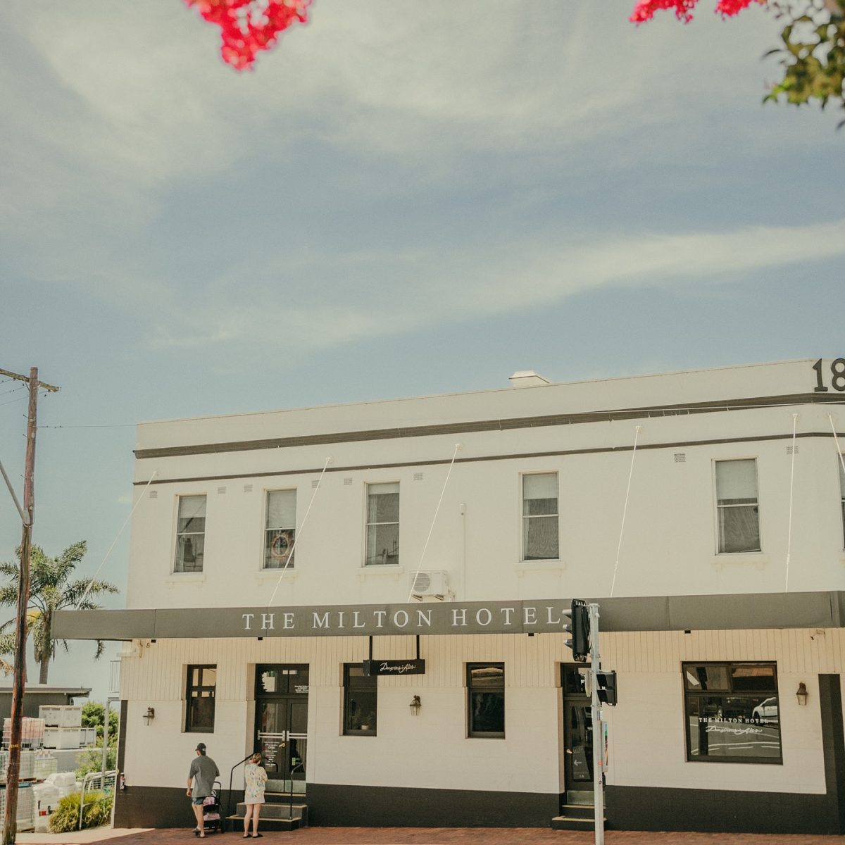 The exterior of The Milton Hotel with some leaves and flowers in the foreground. 