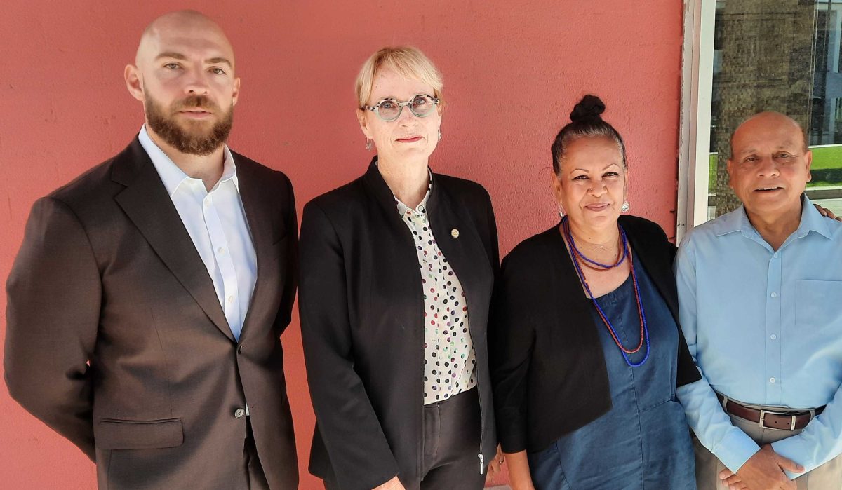 four people standing against an ochre wall