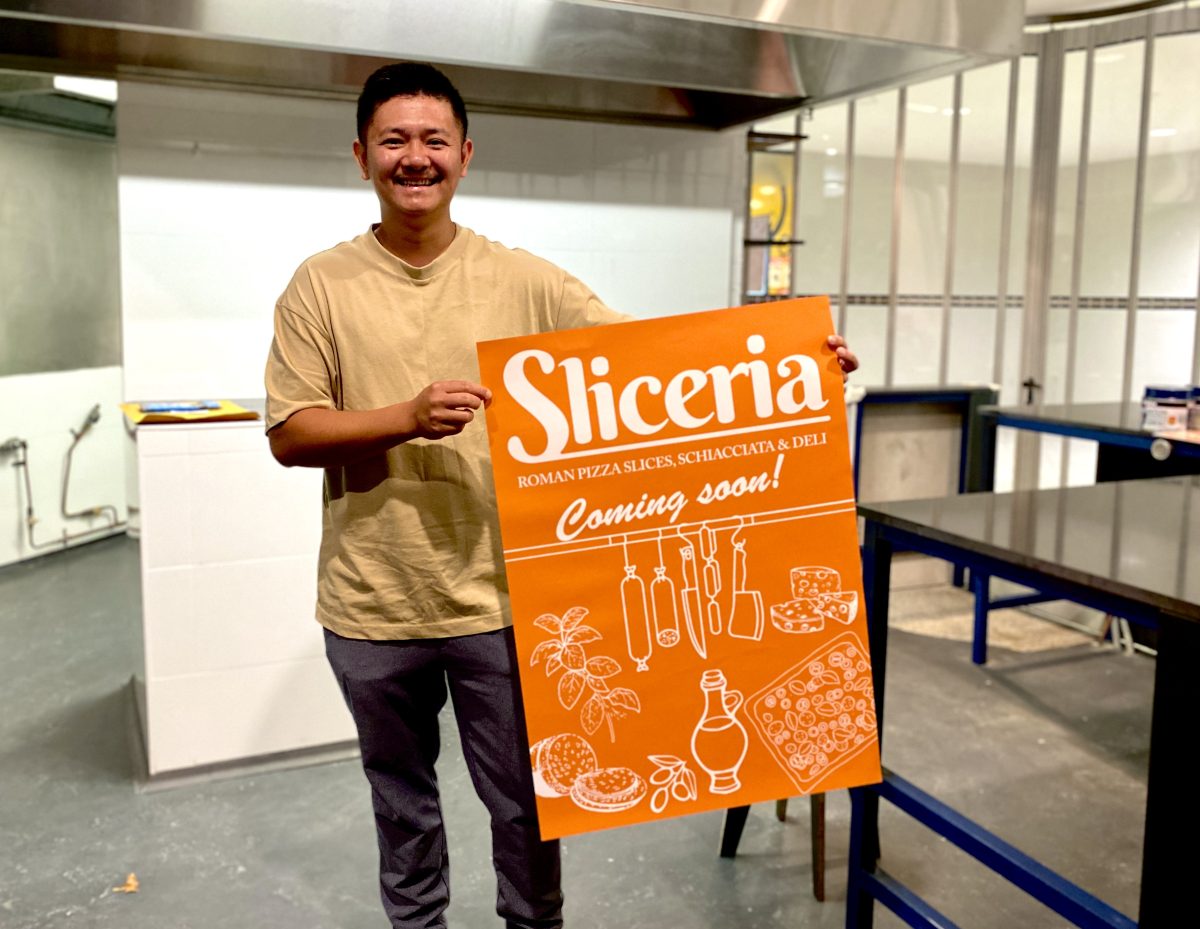 A man holds a large orange sign reading Sliceria Coming Soon!