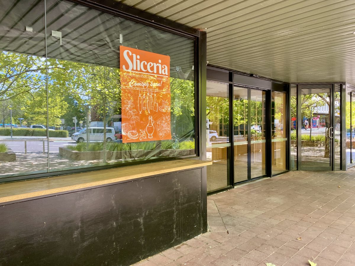 An orange sign reading Sliceria Coming Soon! hangs in a window covered in construction paper.