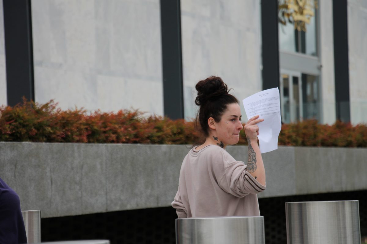 A woman with dark hair and tattoos holding a paper up in an attempt to cover her face