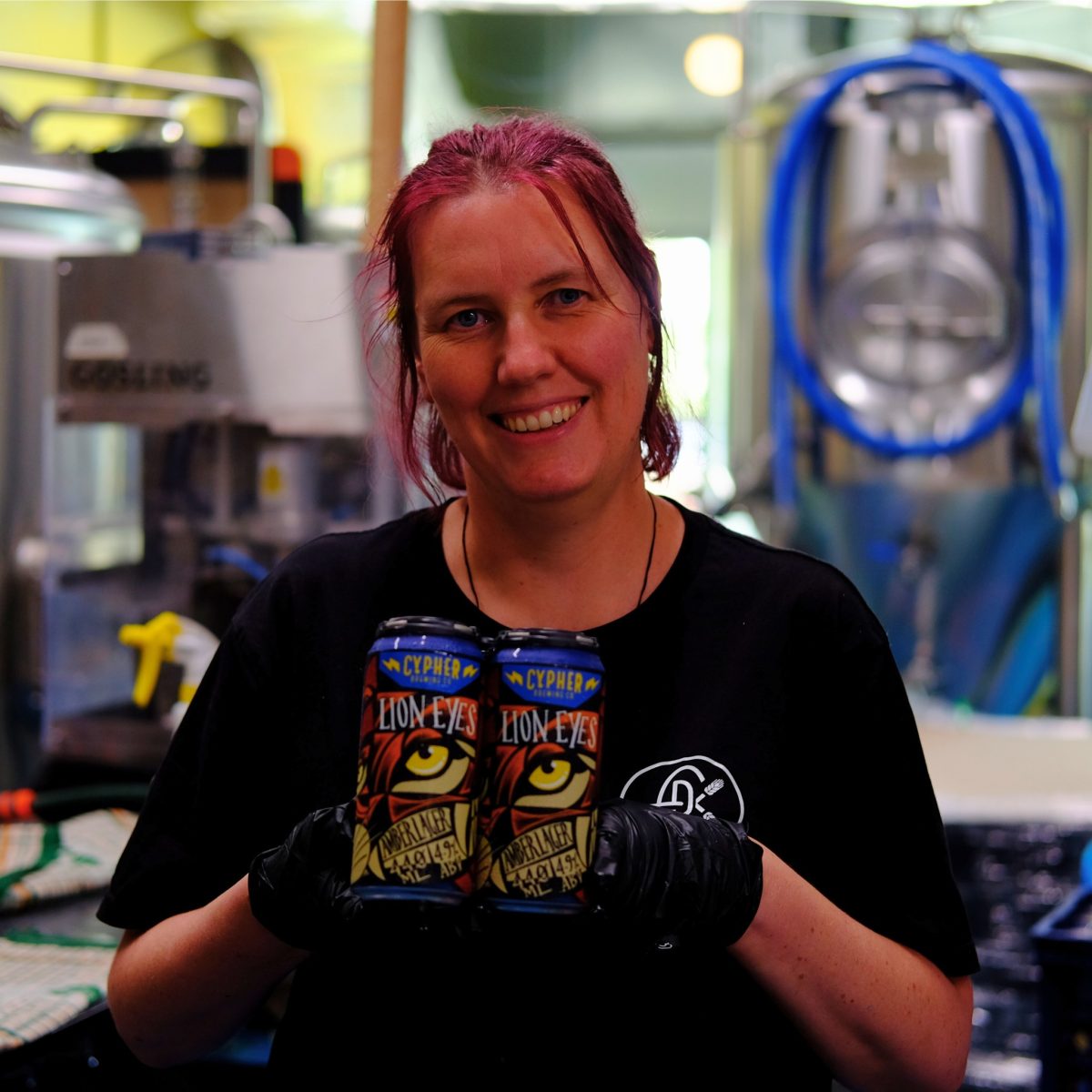 Brewer Lucy Shorrock with pink hair holds a four pack of beers