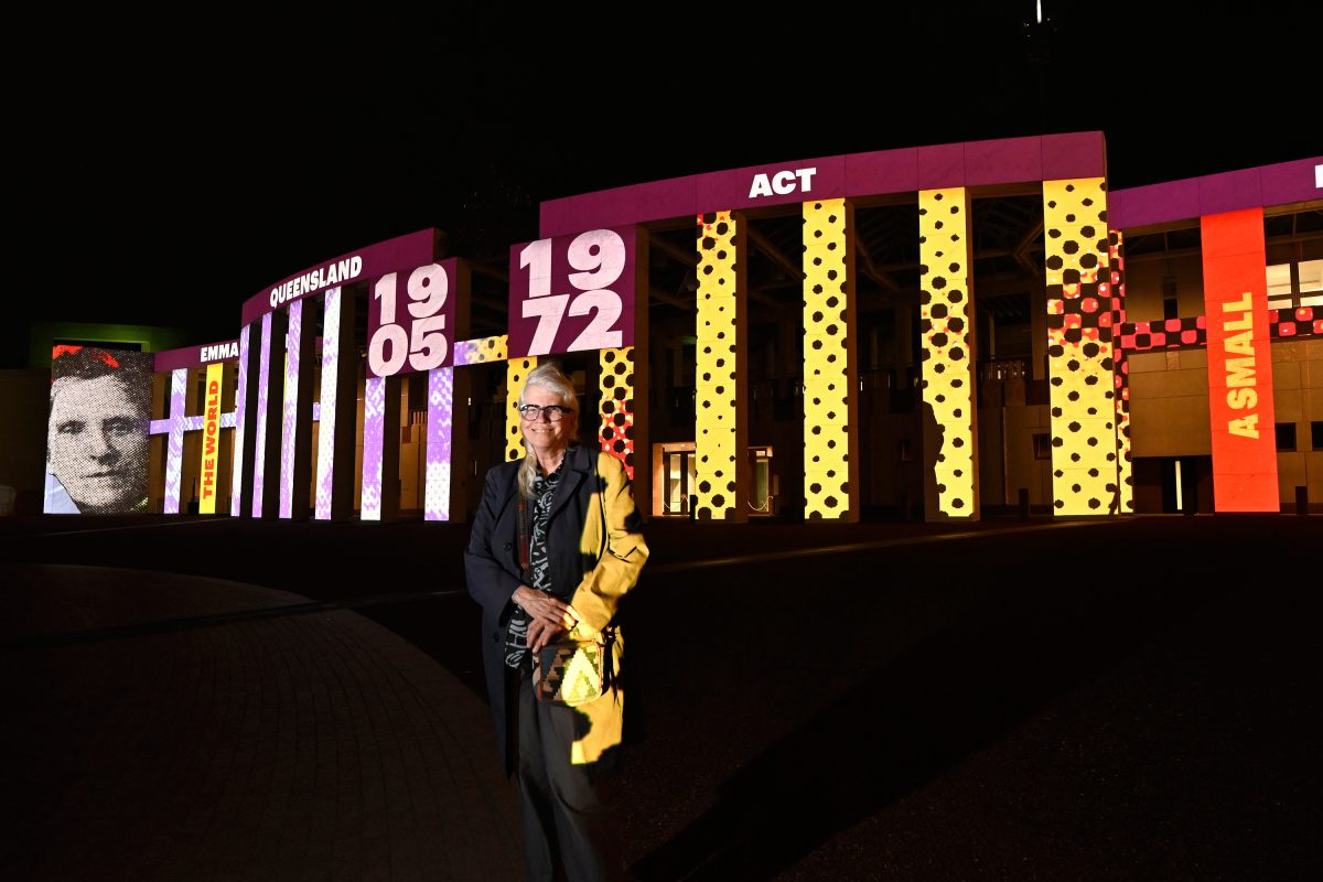 Alison Alder standing in front of her artwork, projected onto Parliament House