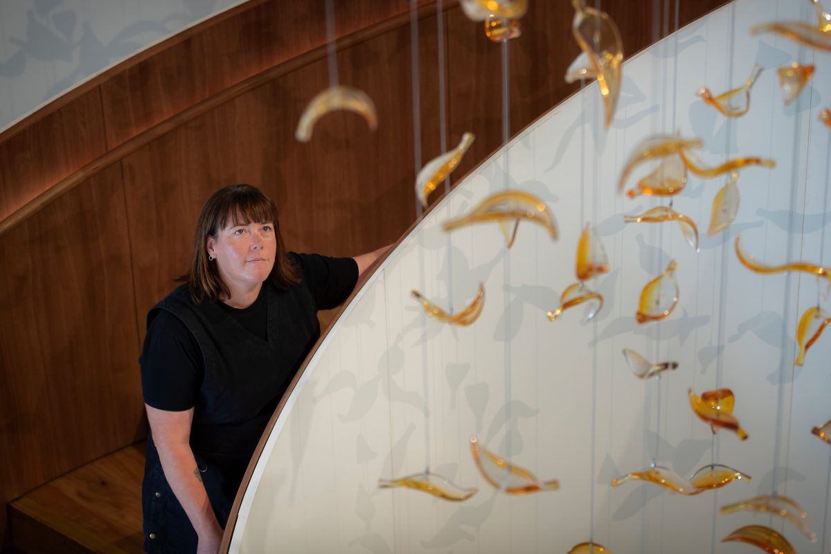 A woman standing in a stairwell, looking up at hanging artwork