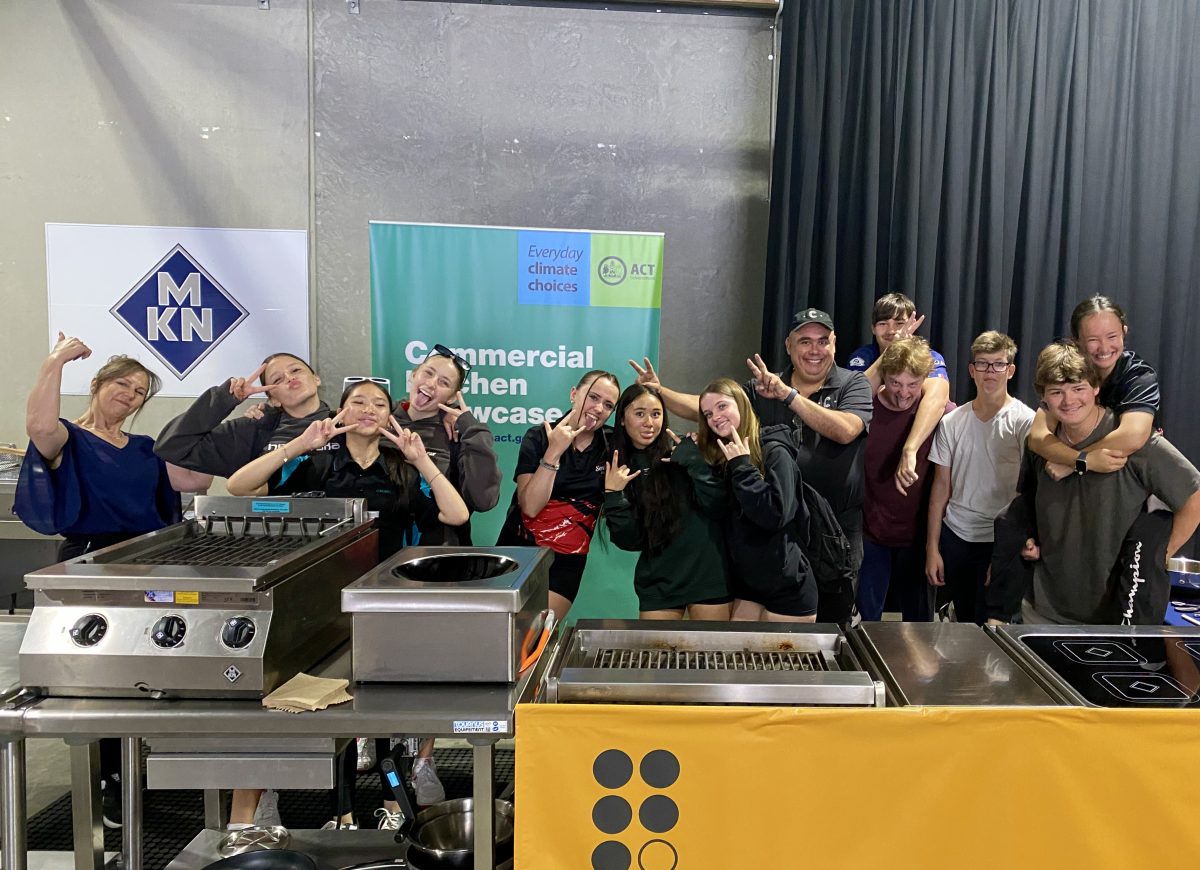 A 'silly' photo of students and staff standing behind a commercial kitchen set up. 