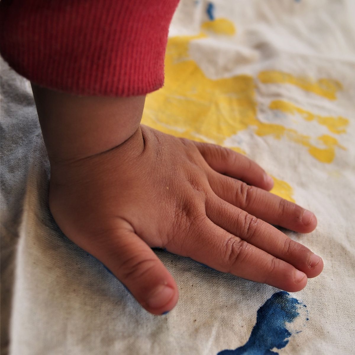 An Indigenous child's hand pushing down on some painted cloth.