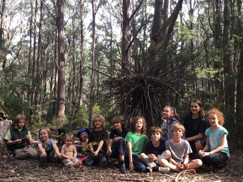 Group of home school students sitting on forest floor.