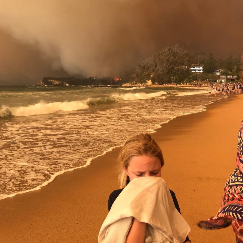 Girl covering face at Malua Bay beach with bushfire in background.