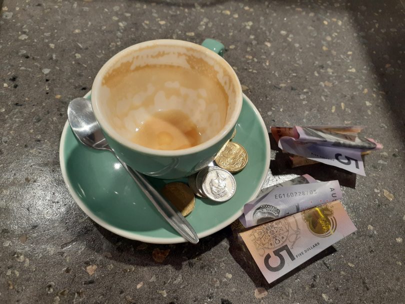 Empty cup of coffee on table with money next to it.