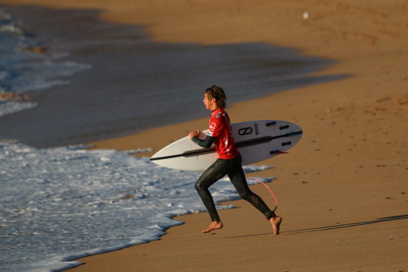 Surfer holding board running on beach towards surf.