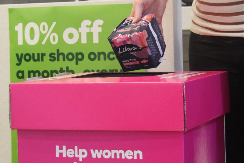 A volunteer drops a donated period pack into the pink box inside Woolworths.