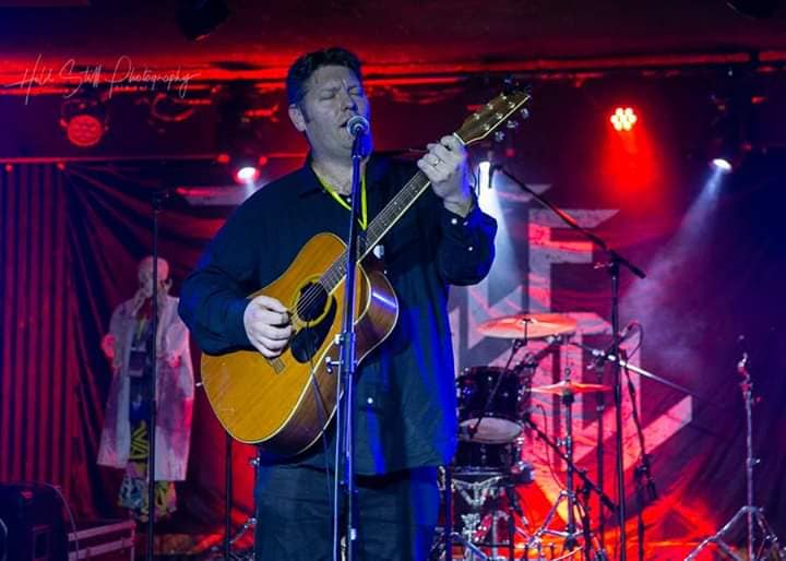 Daniel Kelly performing with guitar onstage at Questfest