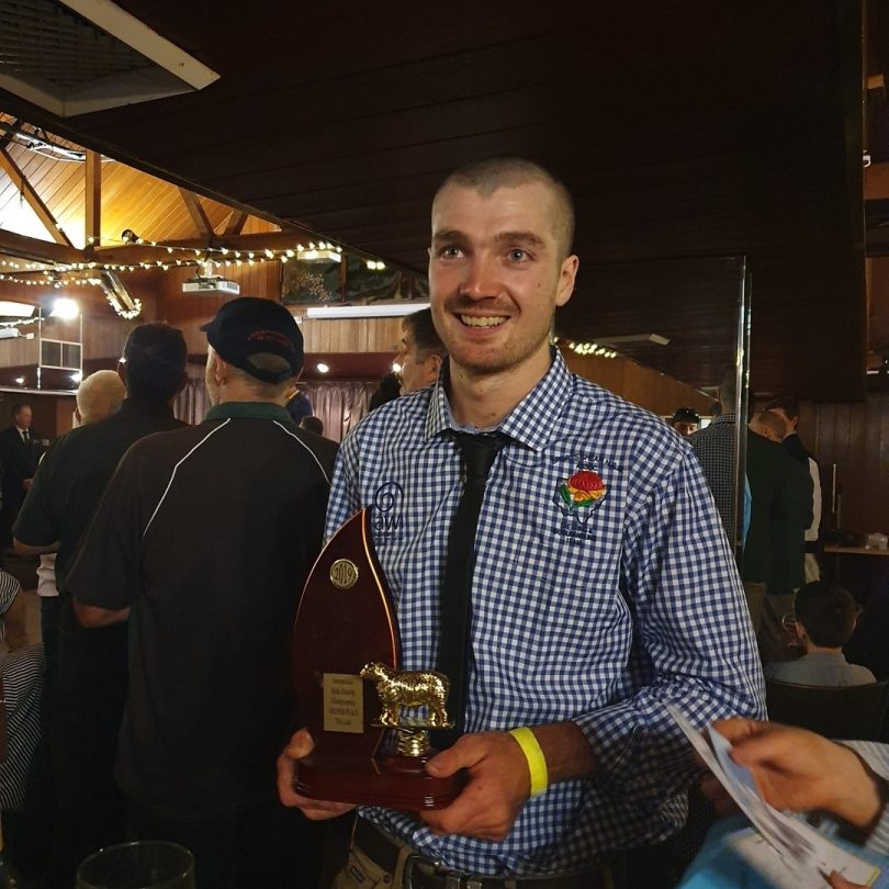 Sam with shaved head and beard holding trophy