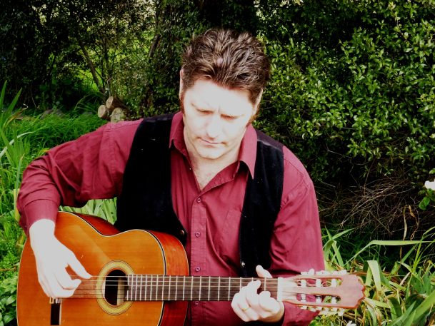 Daniel Kelly playing acoustic guitar outdoors