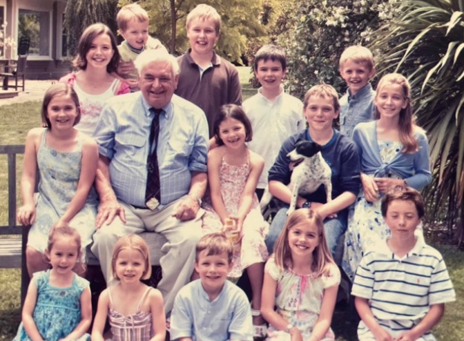 old photo of man surrounded by his 14 grandchildren