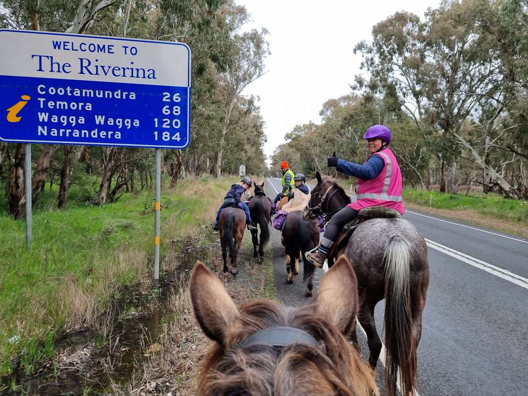 Riders with horses in front of Riverina sign