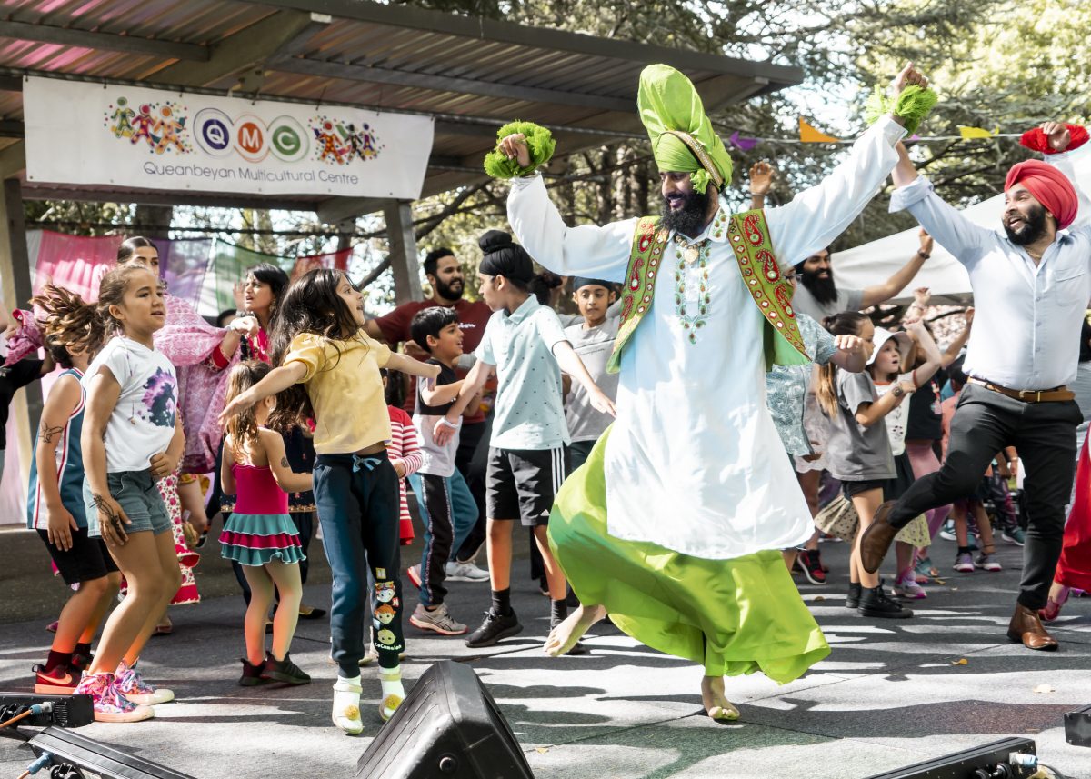 A cultural dancer and some children dance on a stage in front of the Queanbeyan Multicultural Festival crowd.