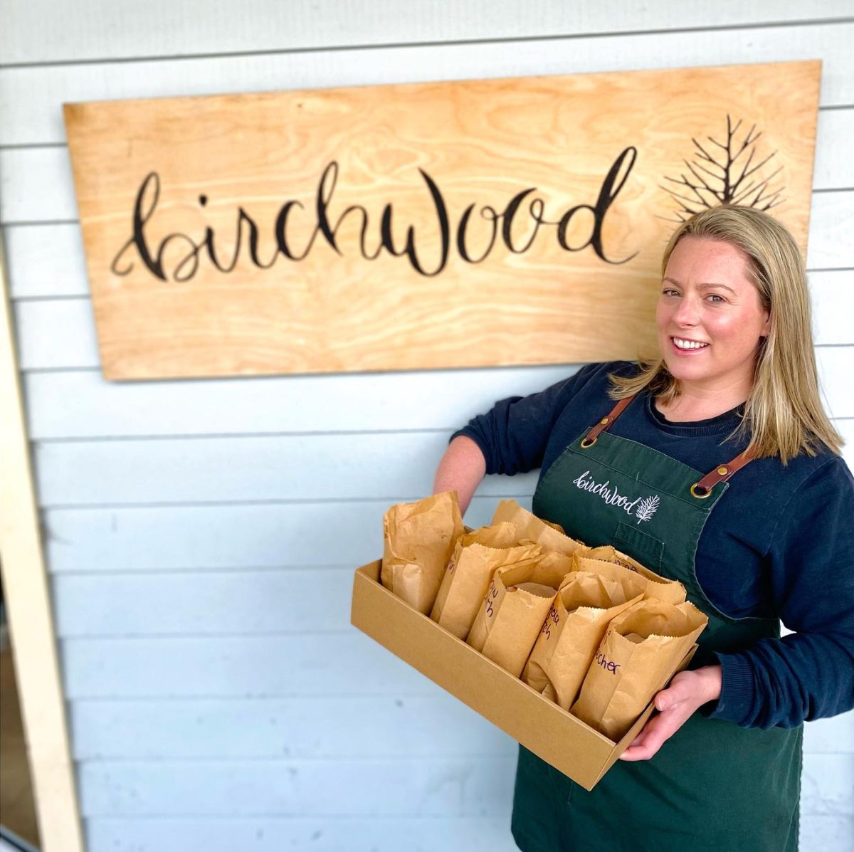 A woman standing in front of a sign and holding a tray of food