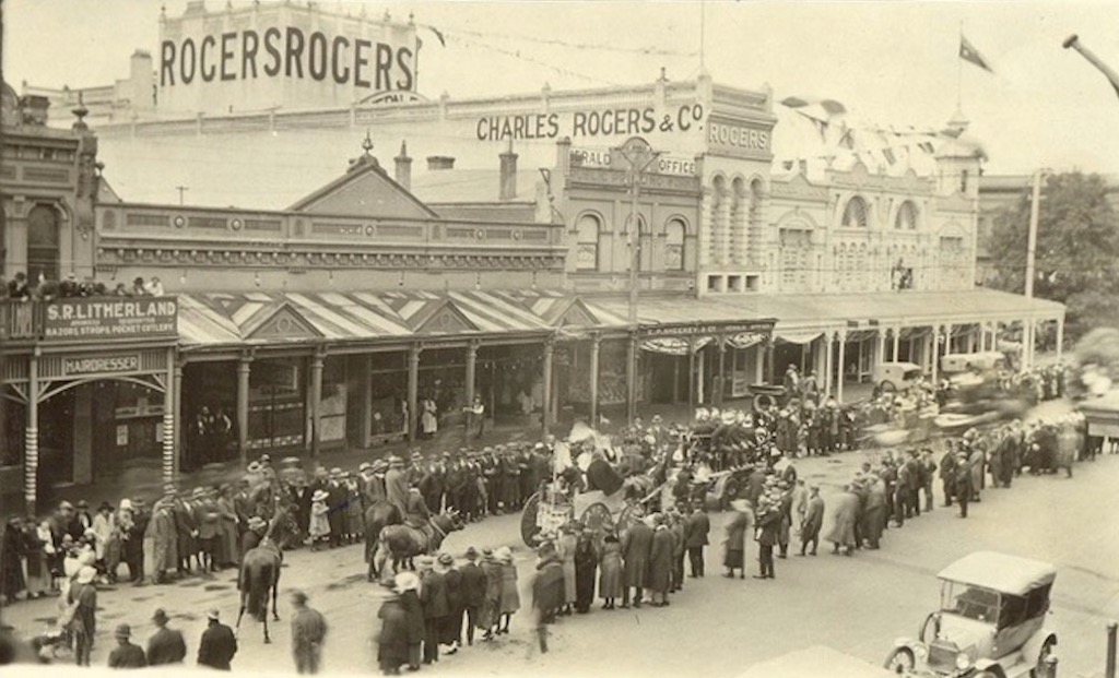 old photo of a crowd watching a parade through a town's high street