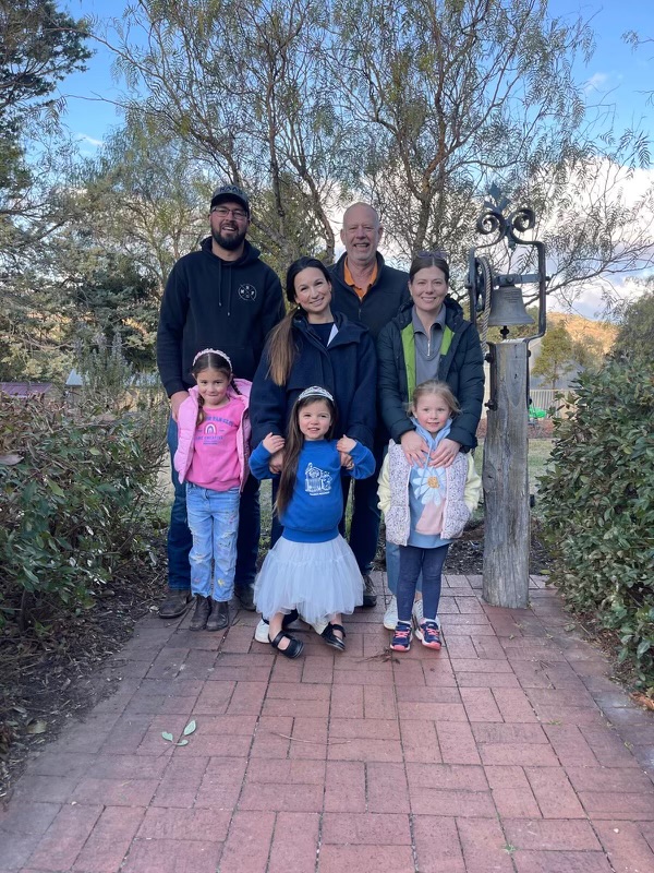 Group of adults and kids in school garden in front of bell