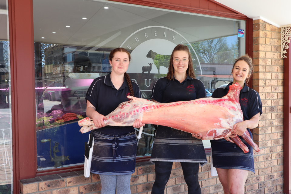 three women holding a lamb carcass