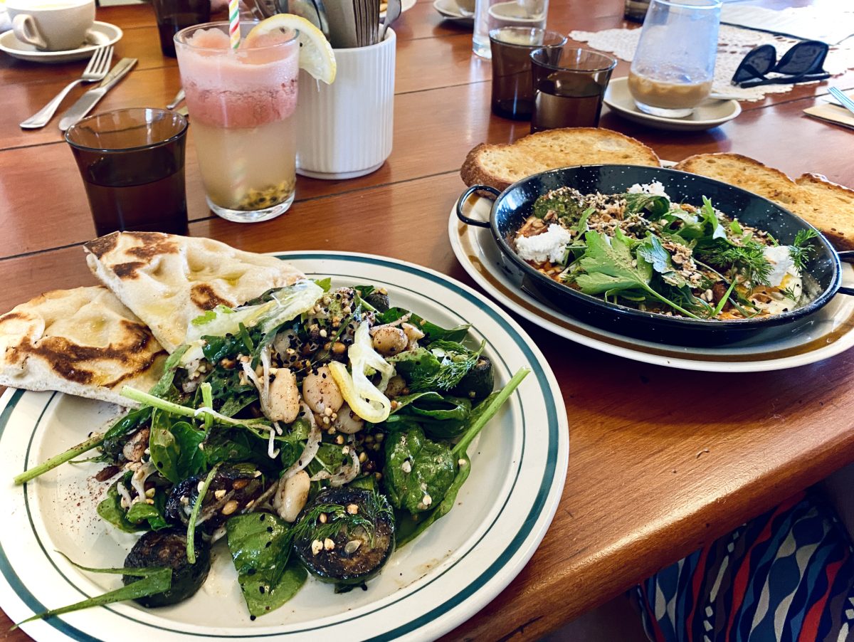 A plate of salad with flatbread and a baked eggs dish in the background.