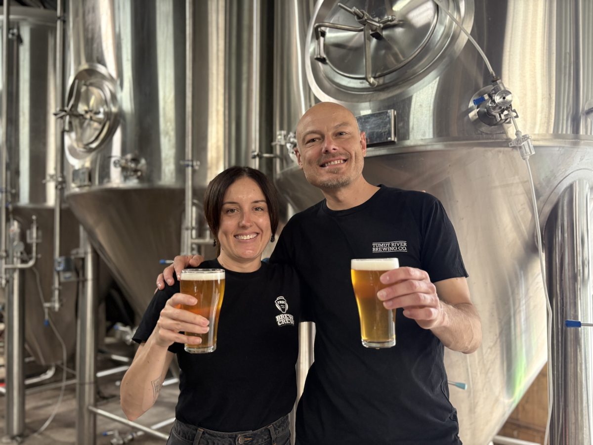 Two people hold beers and wear Tumut River Brewing Co branded shirts