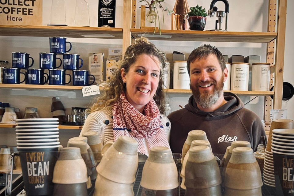 Two people smile at camera from behind barista station.