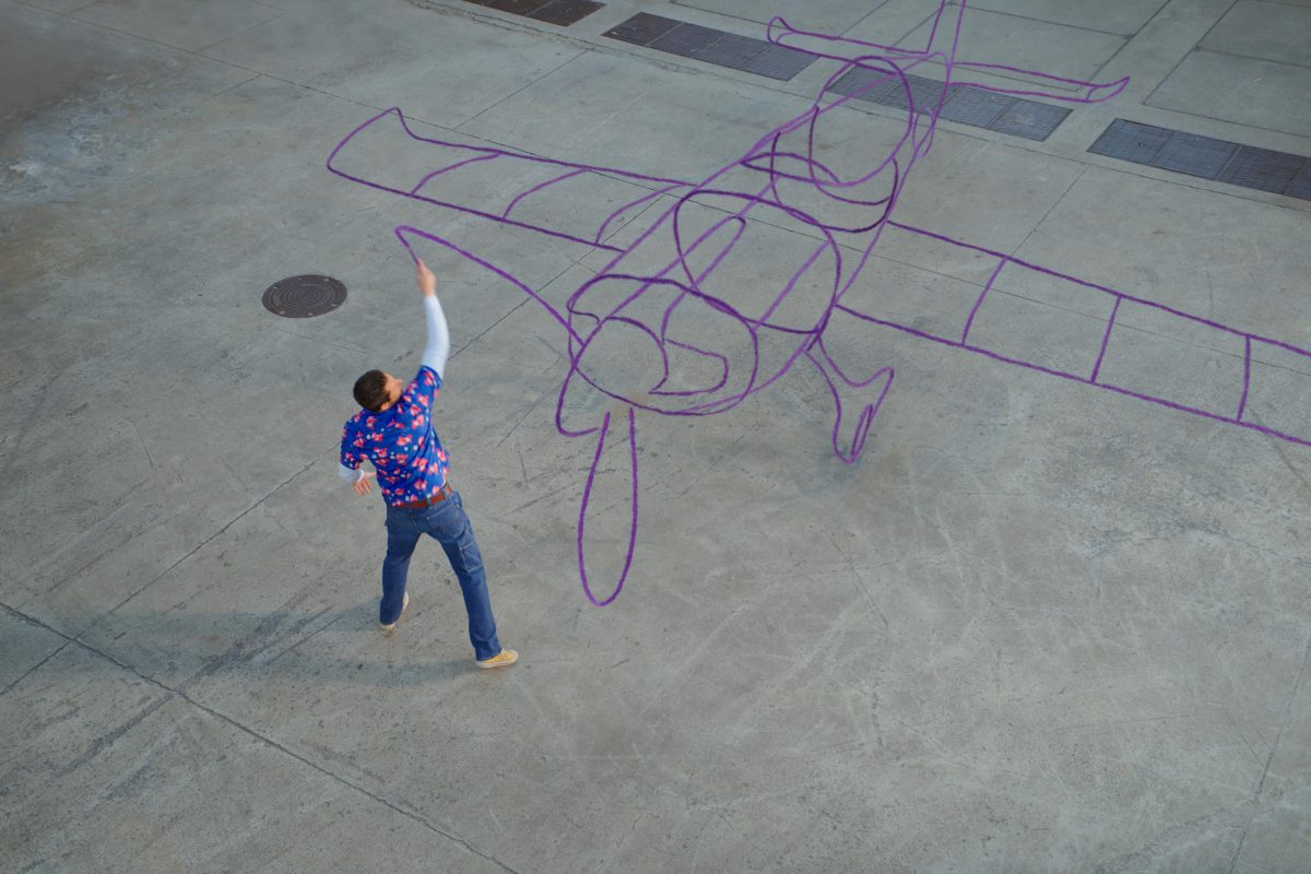 a man drawing on the ground with a purple crayon