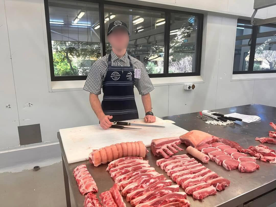 a man standing at a counter with knives and cut-up meat